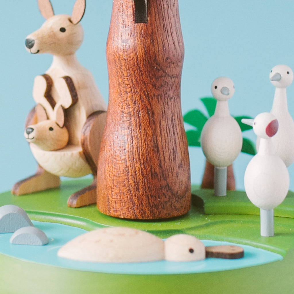 Wooden animal toys including a kangaroo, rabbit, and ducks on a green base with a blue sky background.