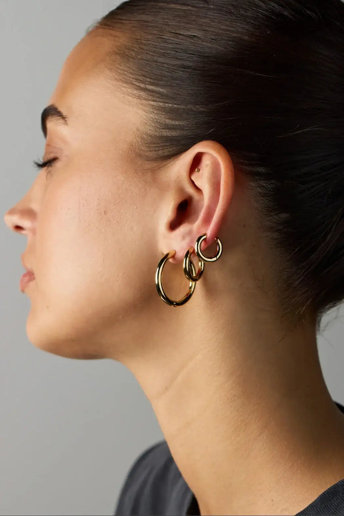 Close-up of a person wearing gold hoop earrings against a neutral background