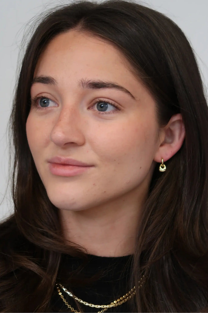 Close-up of a person with long dark hair and gold earrings against a plain background