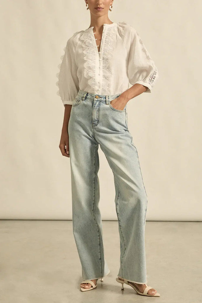 Person wearing a white blouse with lace details and light blue jeans on a neutral background