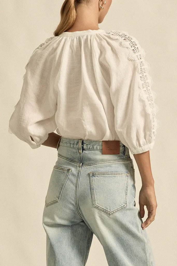 Person wearing a white blouse with lace details and light blue jeans on a beige background