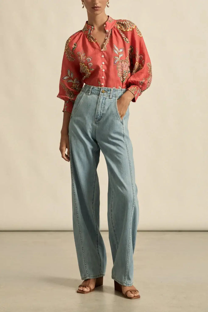 Person wearing a red patterned blouse and light blue jeans against a neutral background