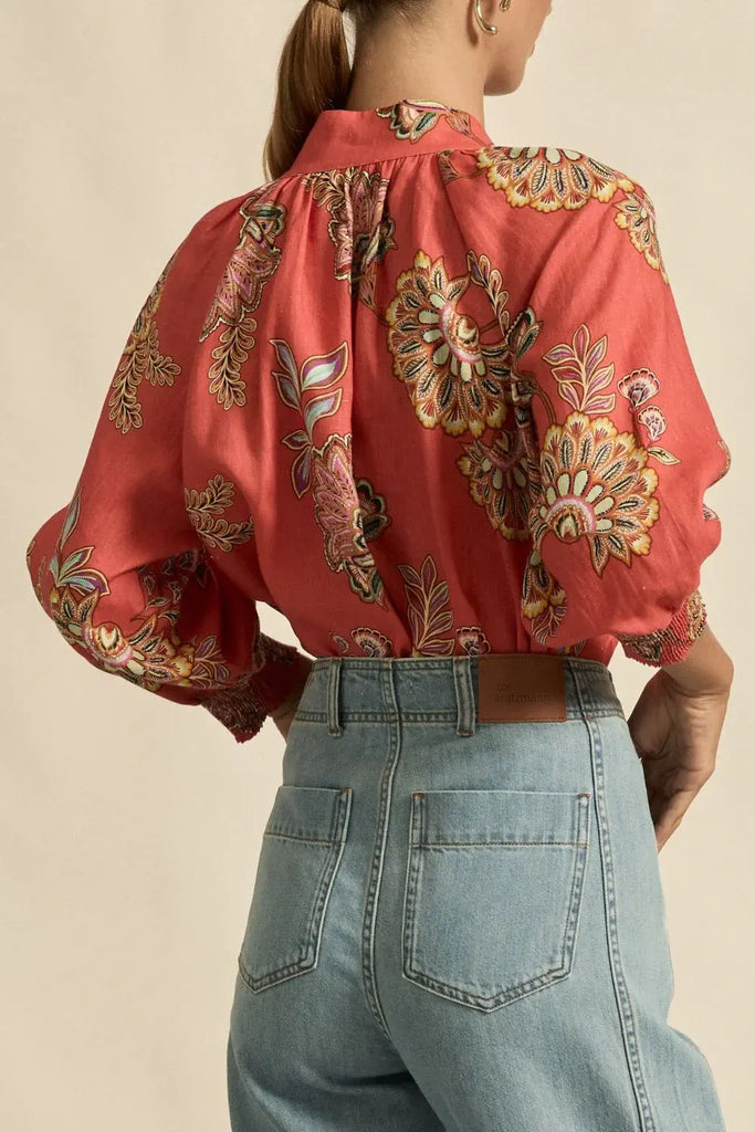 Person wearing a red floral blouse and blue jeans on a beige background