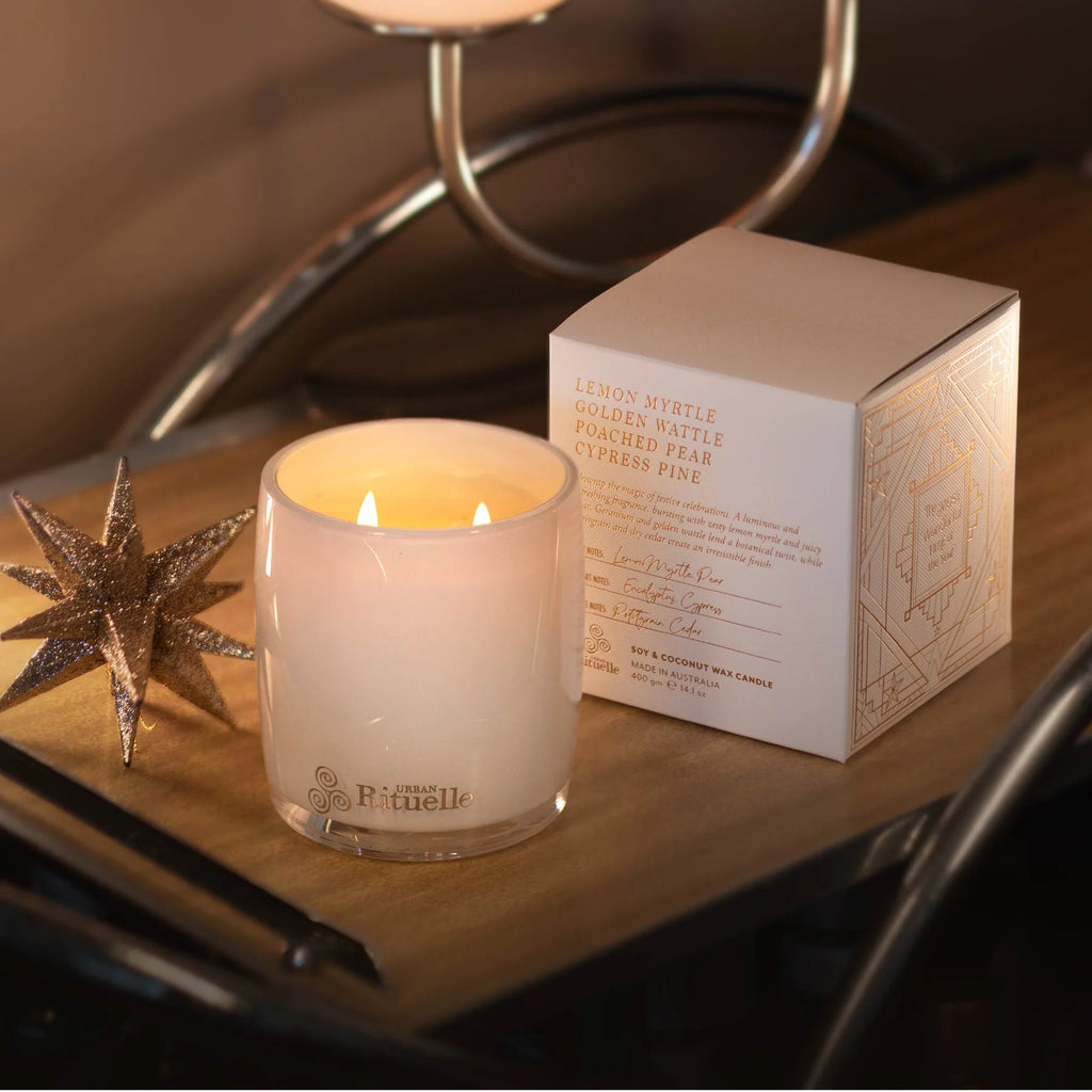 Lit candle in a glass holder next to its packaging on a wooden surface