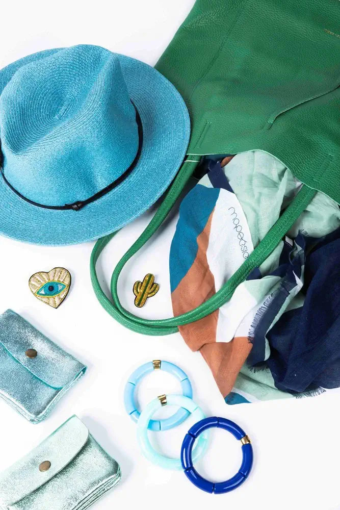 Collection of accessories including a blue hat, green bag, jewelry, and clothing on a white background