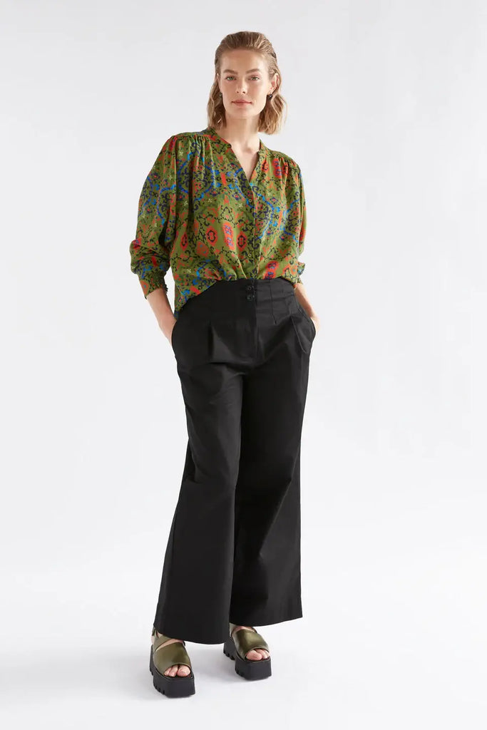 Woman wearing a patterned blouse and black wide-leg pants on a white background