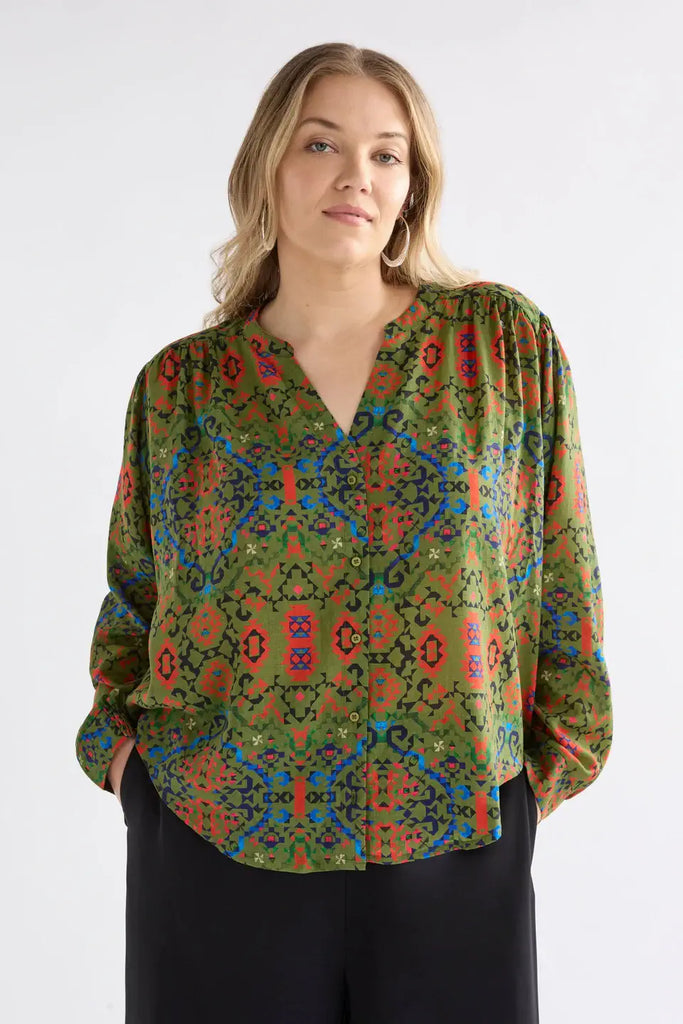 Woman wearing a colorful patterned blouse against a white background