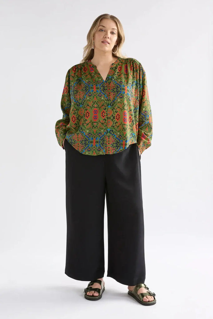 Woman wearing a patterned blouse and black pants on a white background