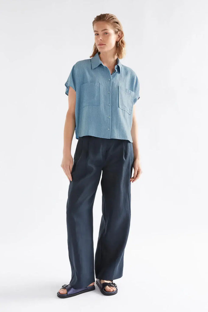 Woman wearing a blue shirt and dark pants on a white background