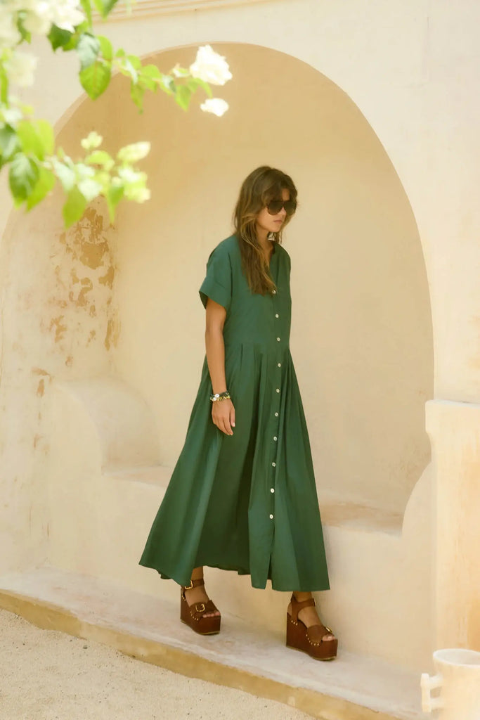 Woman in a green dress standing under an archway with floral decorations.