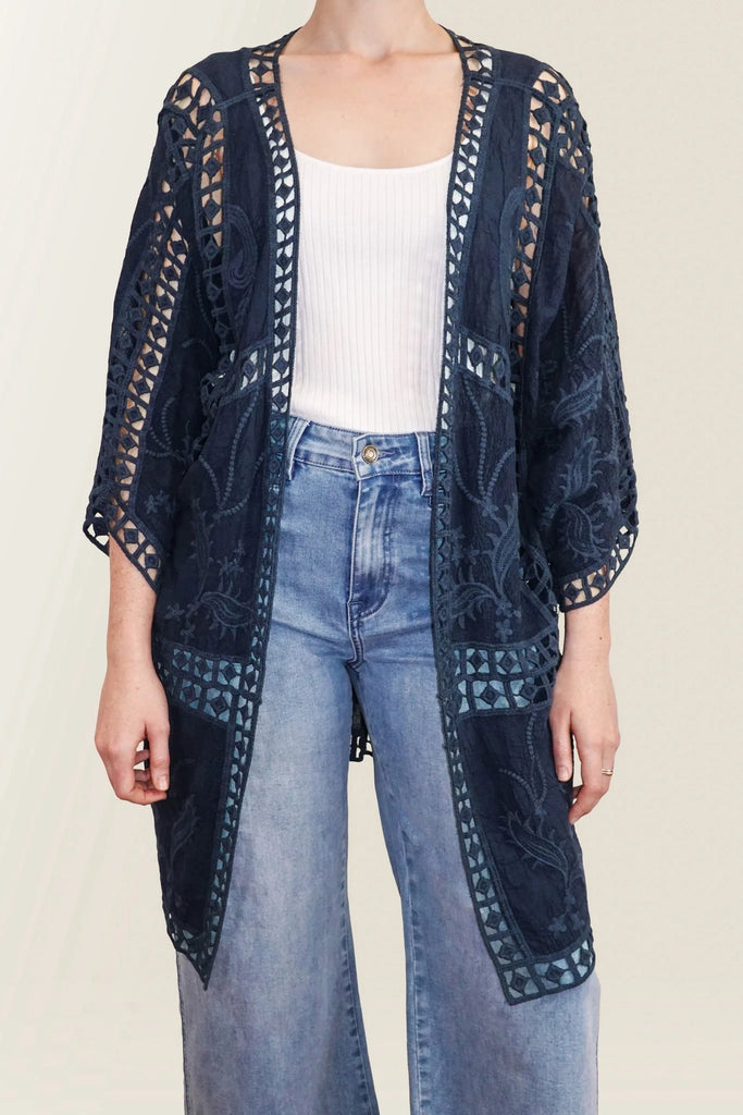 Navy blue embroidered cardigan over a white top and blue jeans on a plain background