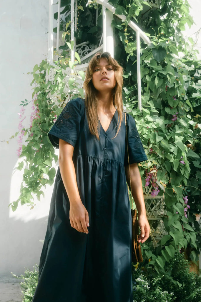 Woman wearing a dark blue dress standing in front of greenery