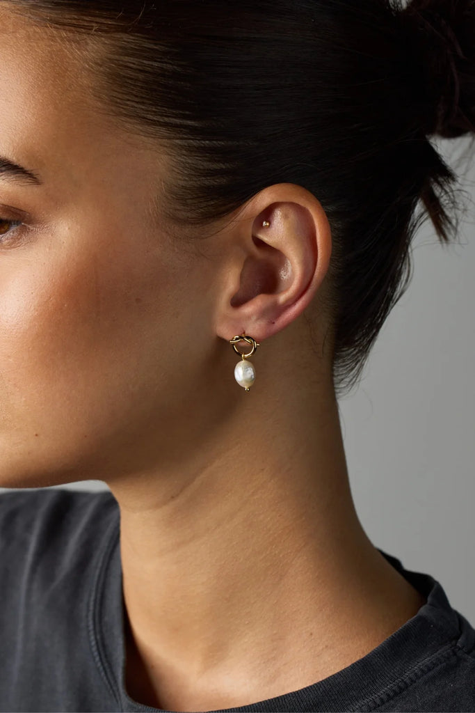 Close-up of a person wearing a pearl earring against a neutral background