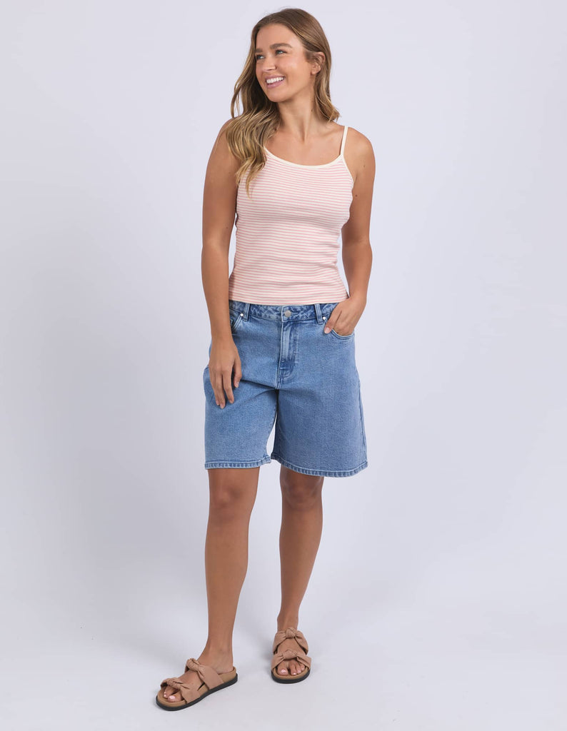 Woman wearing a pink tank top and blue denim shorts on a white background