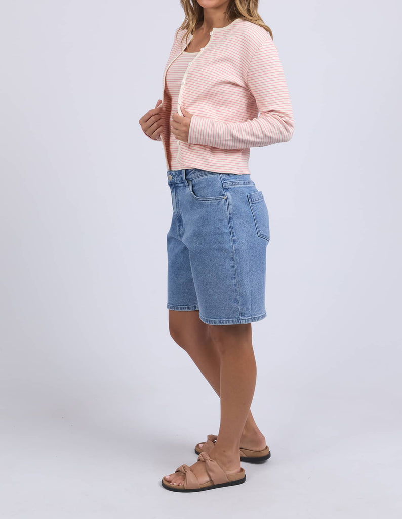 Woman wearing a light pink cardigan and blue denim shorts on a white background