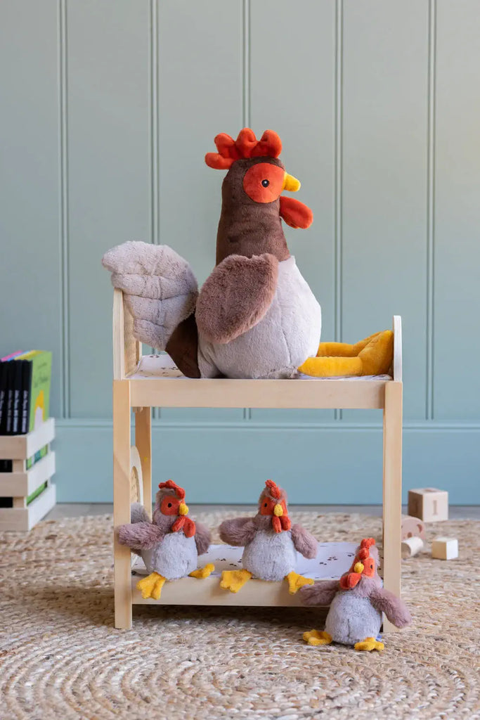 Plush toy chicken on a wooden shelf with more plush chickens below against a light blue wall.