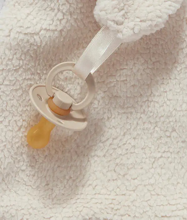 Baby pacifier with a white strap on a soft, textured beige background