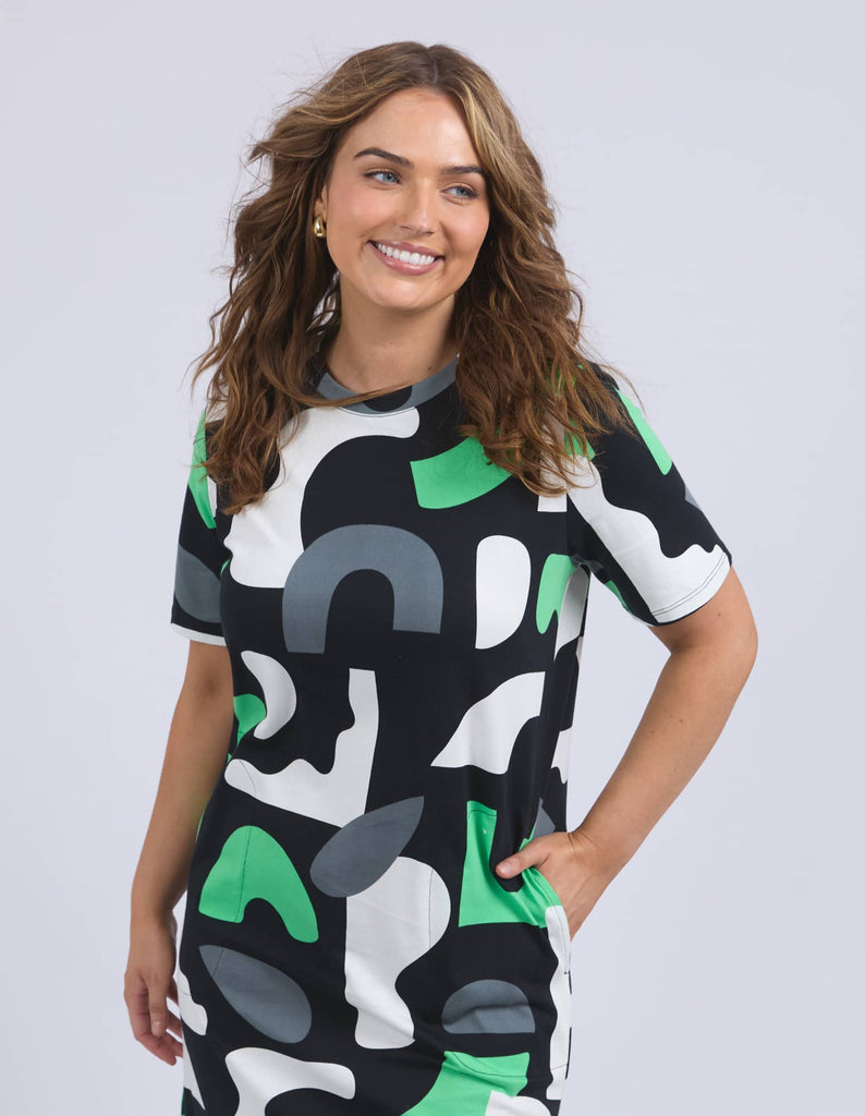 Woman wearing a black, white, and green patterned dress on a plain background